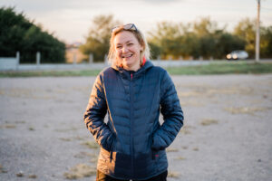 Image of a woman recovering from domestic abuse outside with her hands in her pockets smiling and the sun on her face.